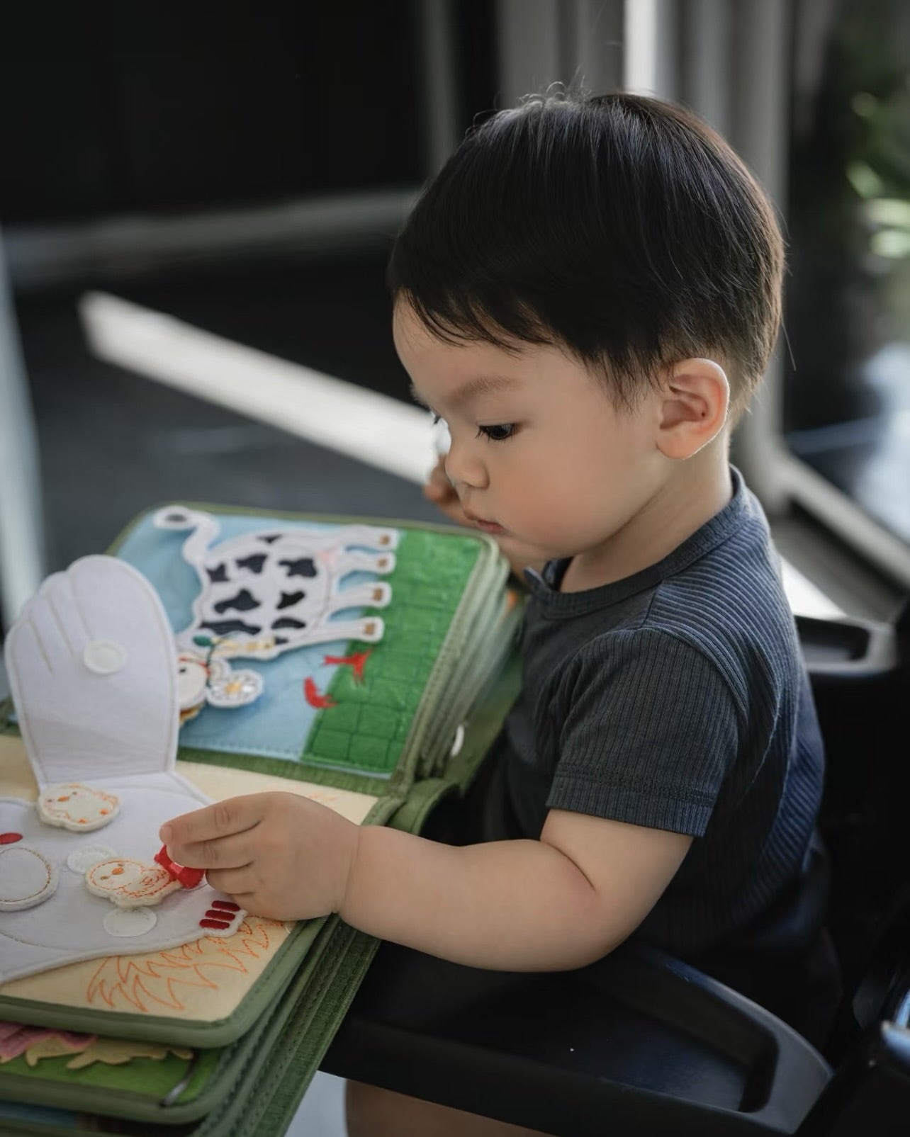 Junge betrachtet konzentriert ein aufgeschlagenes Bauernhof Quiet Book mit Filz-Kuh – Montessori-Stoffbuch von My First Book und Small Hands