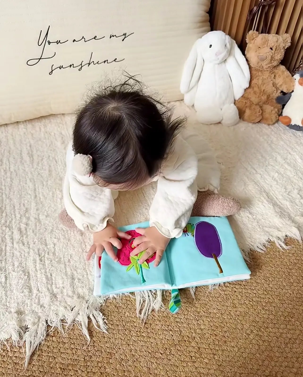 Kleinkind spielt im Kinderzimmer vertieft mit einem Quiet Book, daneben Kuscheltiere – Montessori-Spielzeug im Alltag