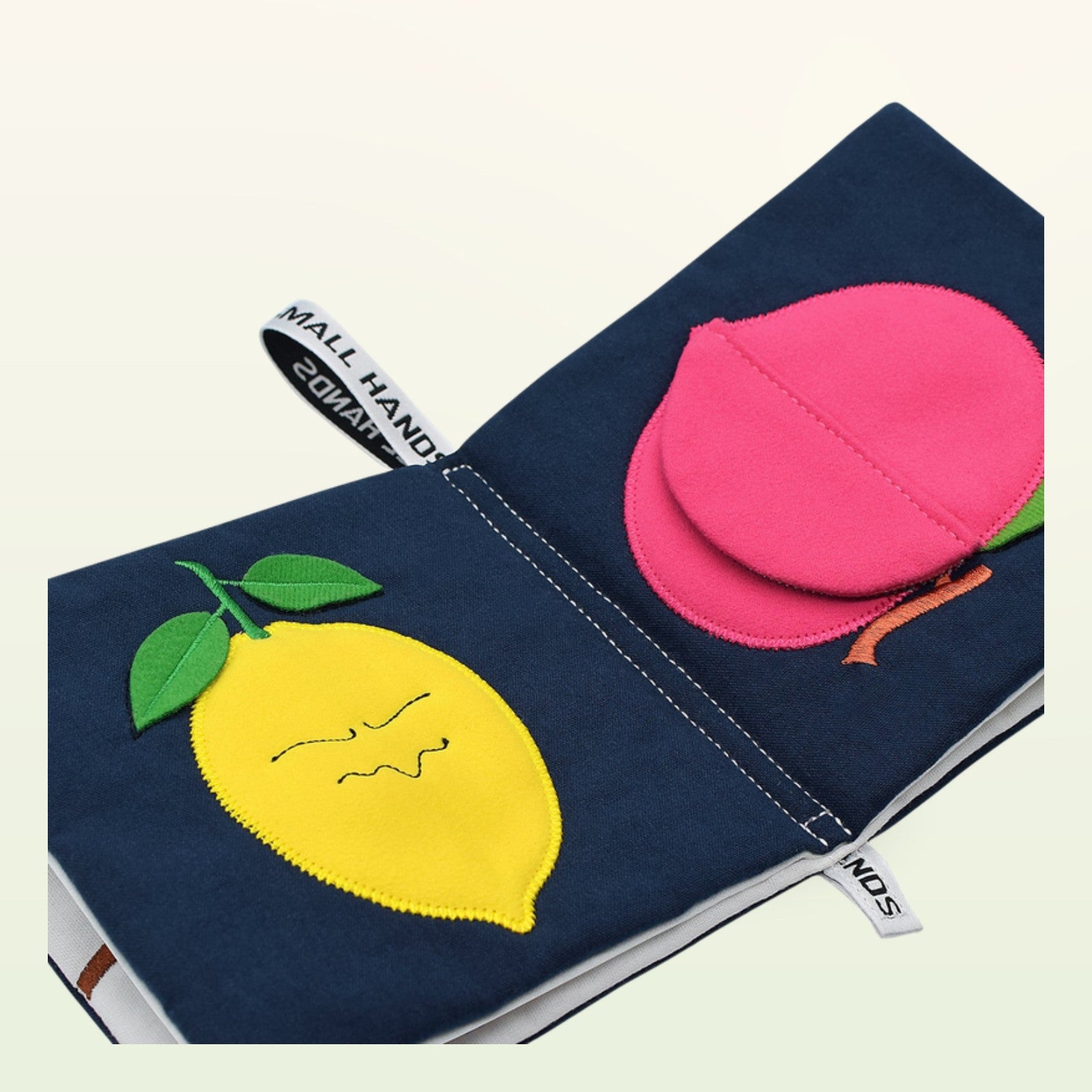 Small Hands Bunte Früchte Montessori Stoffbuch aufgeschlagen – gelbe Zitrone und pinker Pfirsich auf sanftem Creme-Hintergrund – ab 0 Monaten