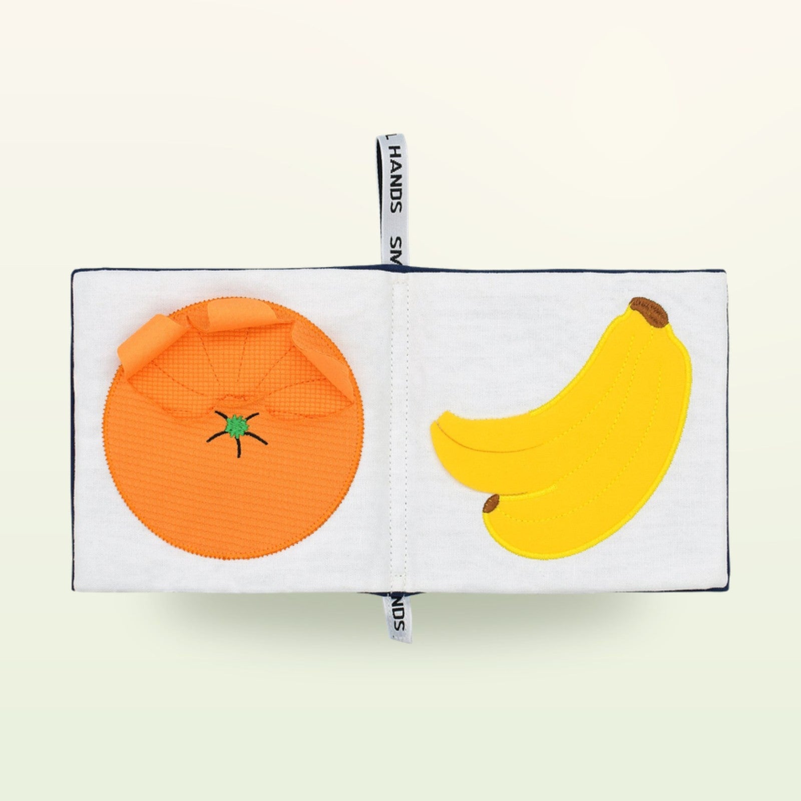 Small Hands Exotische Früchte Montessori Stoffbuch aufgeschlagen – Orange und Banane auf sanftem Creme-Hintergrund – ab 0 Monaten