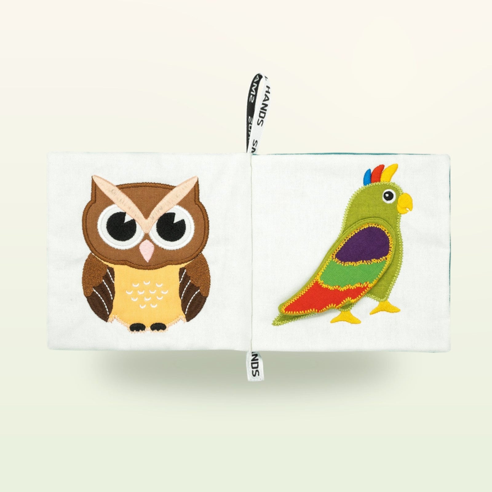 Small Hands Vögel Montessori Stoffbuch aufgeschlagen – braune Eule und bunter Papagei auf sanftem Creme-Hintergrund – ab 0 Monaten