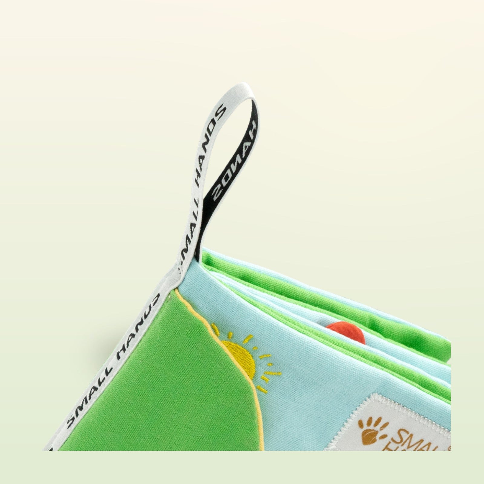My First Book Small Hands Bauernhof Stoffbuch geöffnet mit Aufhänger auf sanftem Wiesengrün-Hintergrund – ab 0 Monaten