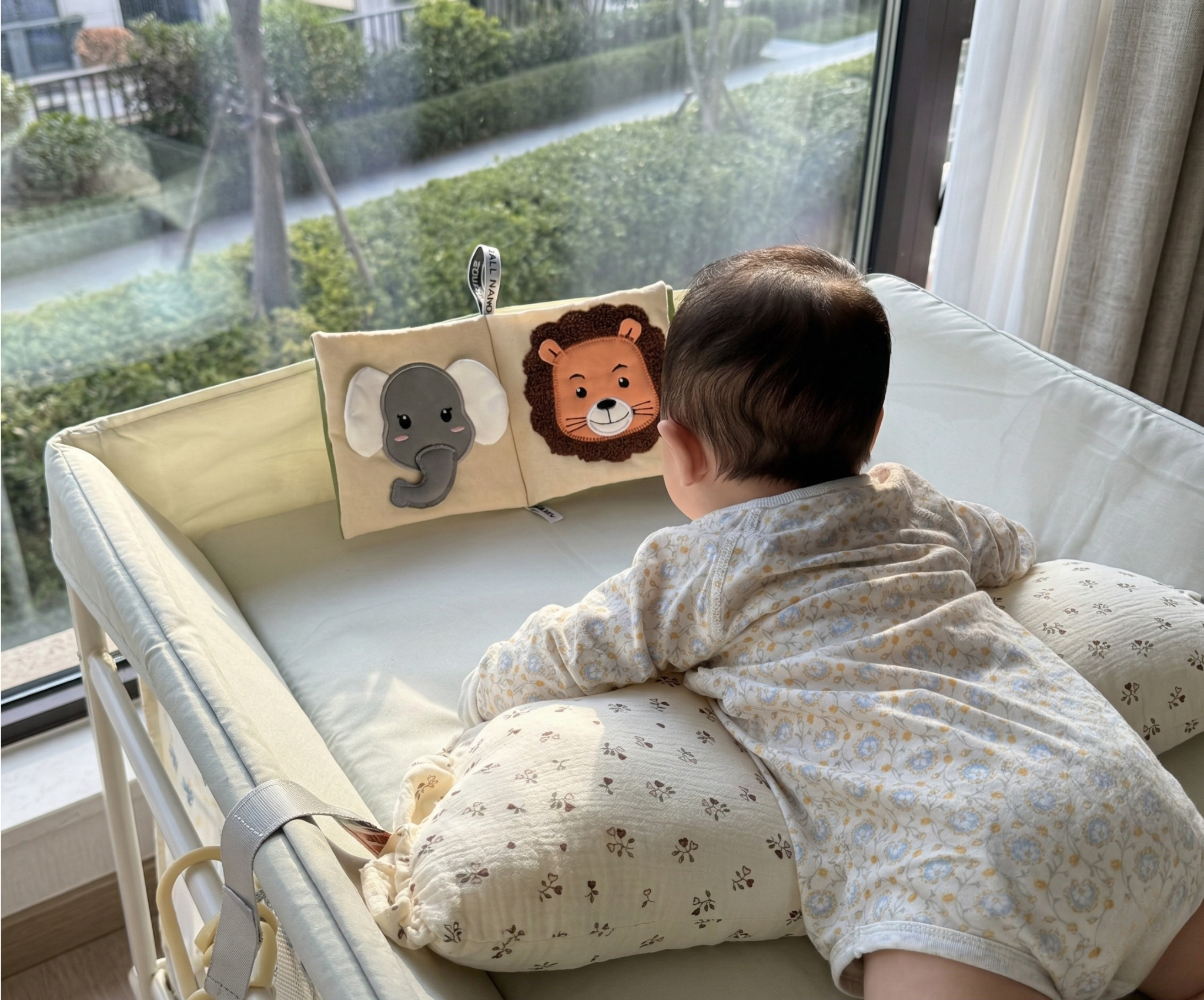 Baby schaut im Bett ein aufgestelltes Small Hands Stoffbuch mit Elefanten- und Löwen-Gesicht an – sinnvolles Montessori-Geschenk zum 1. Geburtstag