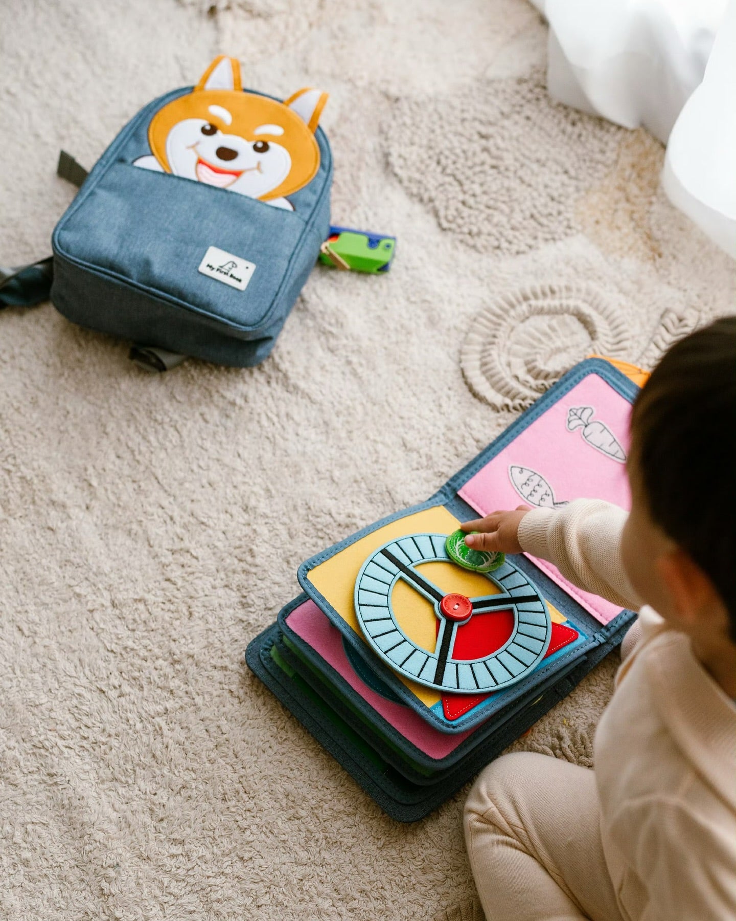Pet Friends Quiet Book mit Hunde-Rucksack auf dem Teppich, daneben spielt ein Kind an einer Filz-Seite – Montessori-inspiriertes Stoffbuch von My First Book