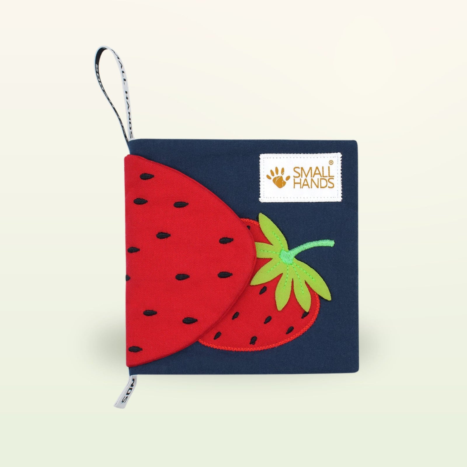 Small Hands Bunte Früchte Montessori Stoffbuch – Einband mit roter Erdbeere und Small-Hands-Schlaufe auf sanftem Creme-Hintergrund – ab 0 Monaten