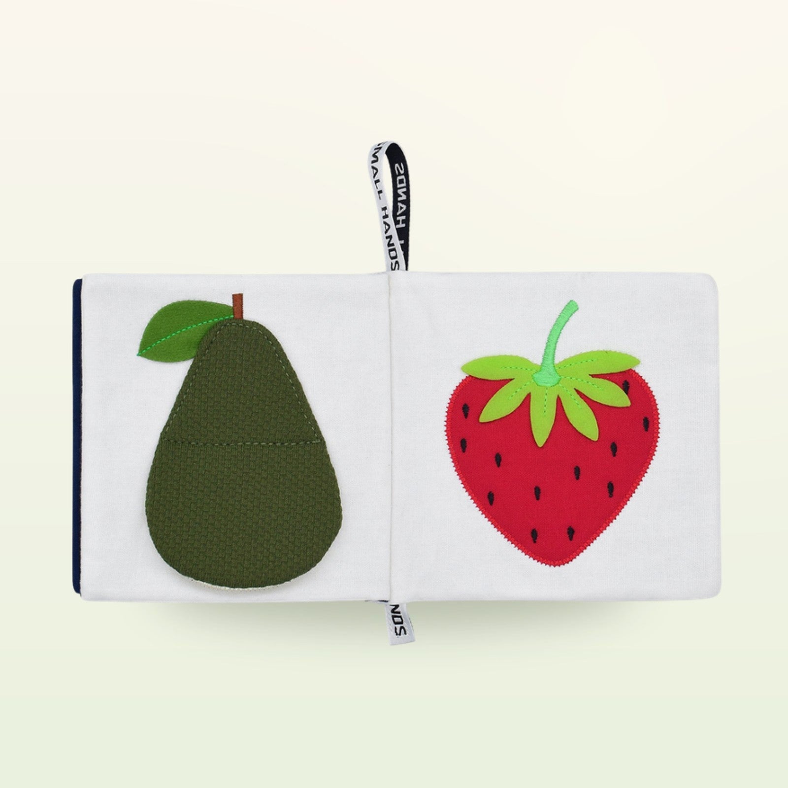 Small Hands Bunte Früchte Montessori Stoffbuch aufgeschlagen – grüne Avocado und rote Erdbeere auf sanftem Creme-Hintergrund – ab 0 Monaten
