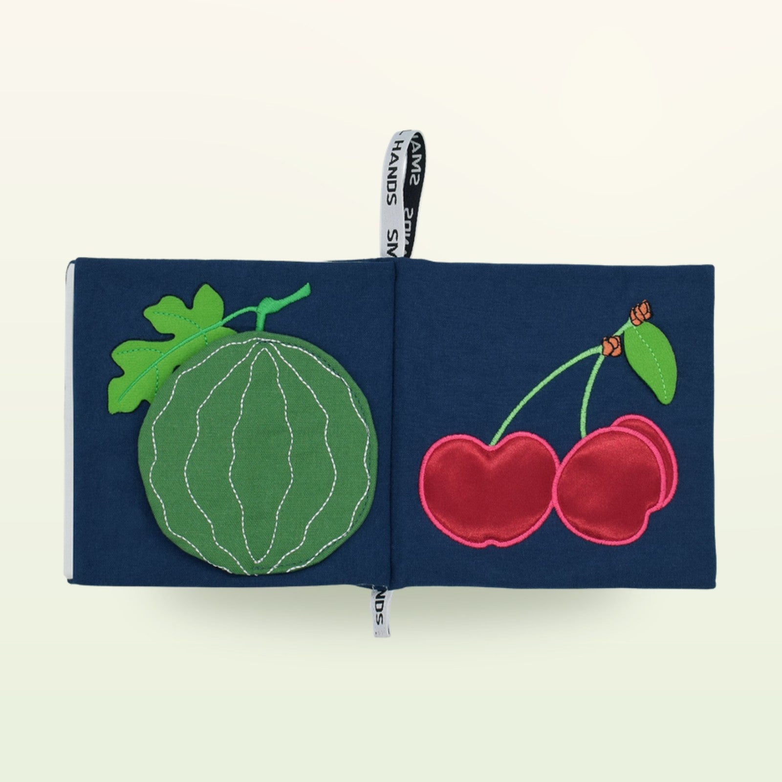 Small Hands Exotische Früchte Montessori Stoffbuch aufgeschlagen – Wassermelone und Kirschen auf sanftem Creme-Hintergrund – ab 0 Monaten
