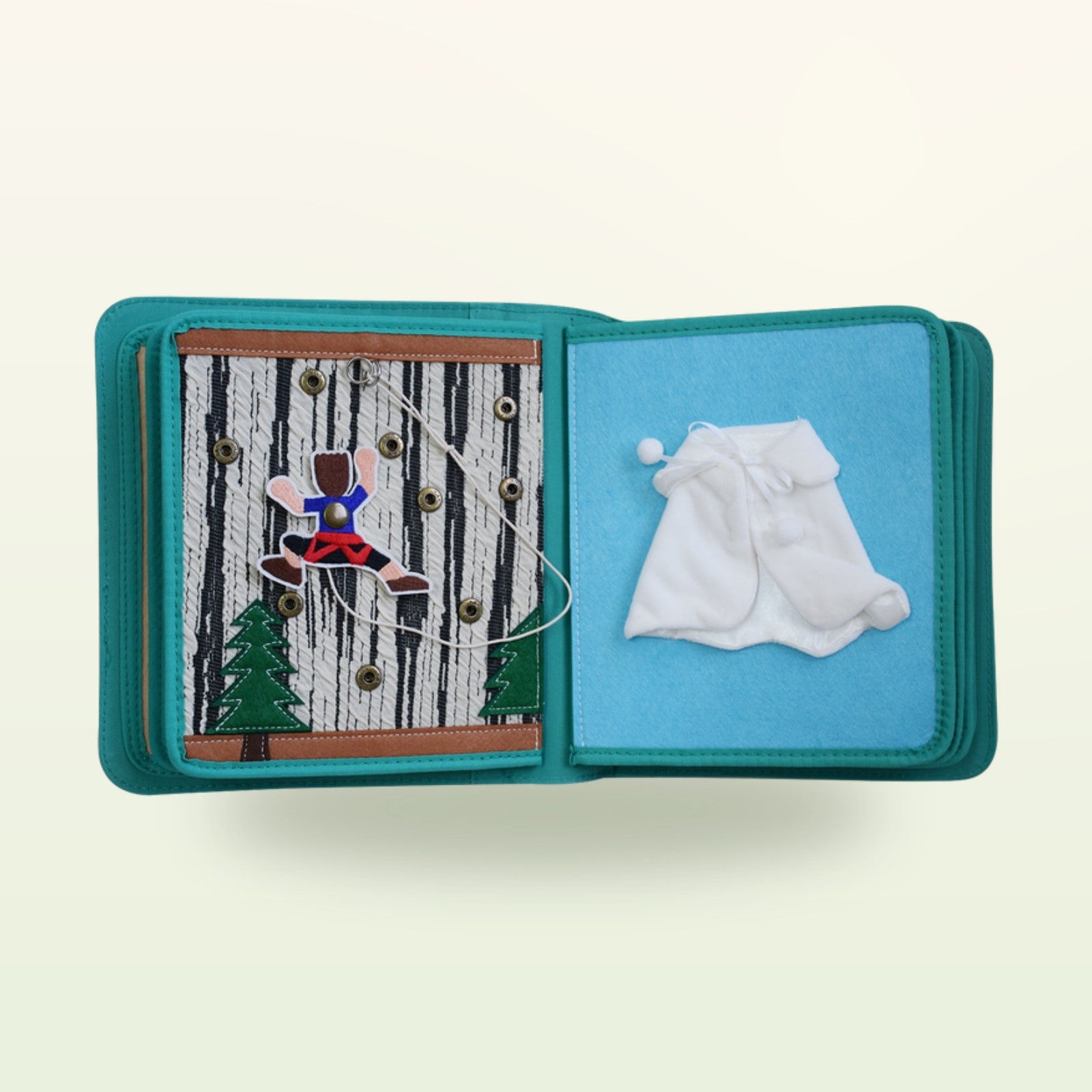 Kleiderschrank Quiet Book Stoffseite mit Fädel-Figur am Baum mit Druckknöpfen und weißem Wintermantel auf sanftem Creme-Hintergrund – ab 3 Jahren