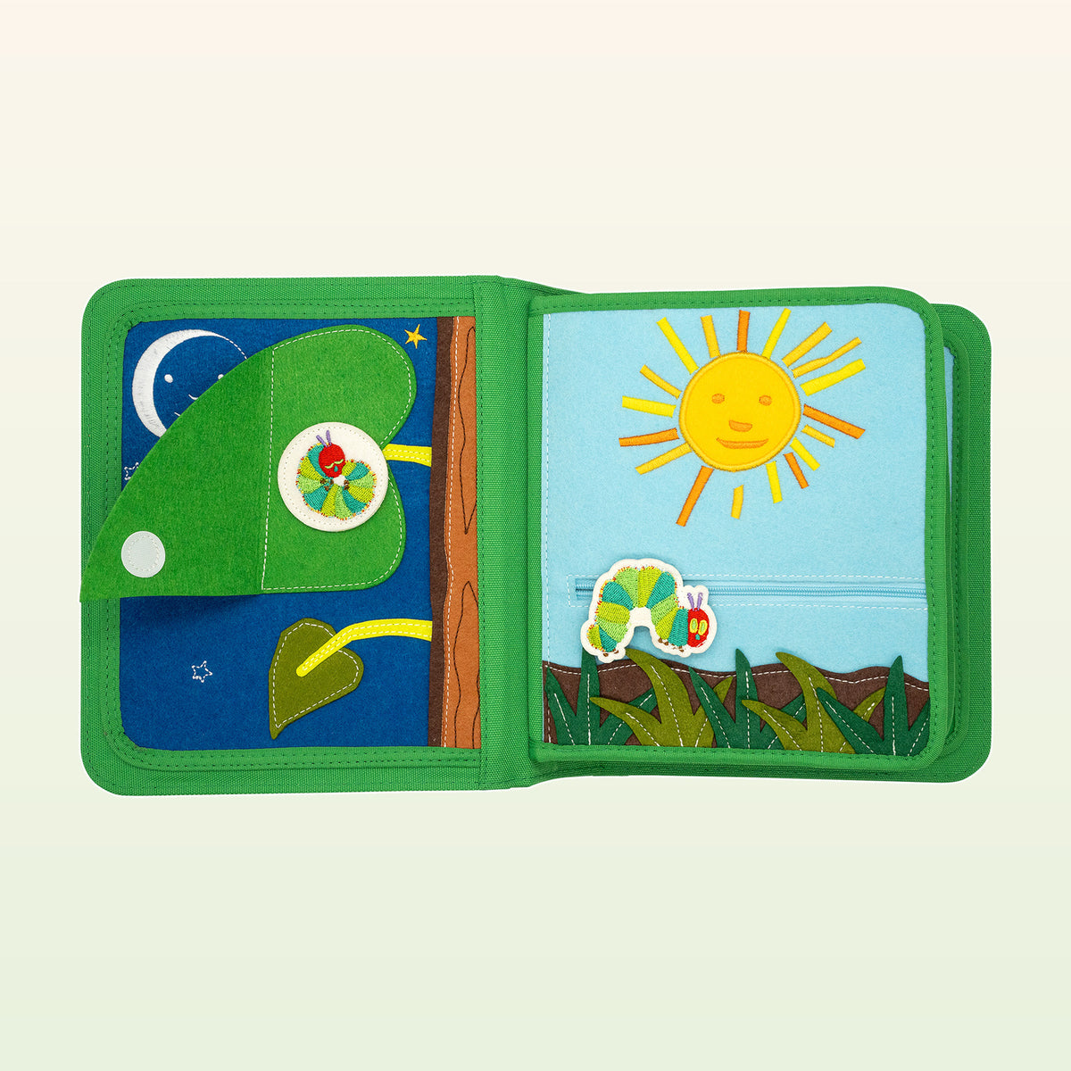My First Book Die Raupe Nimmersatt Quiet Book aufgeschlagen – Doppelseite mit Mond, Blatt und Sonne über dem Gras – ab 1 Jahr
